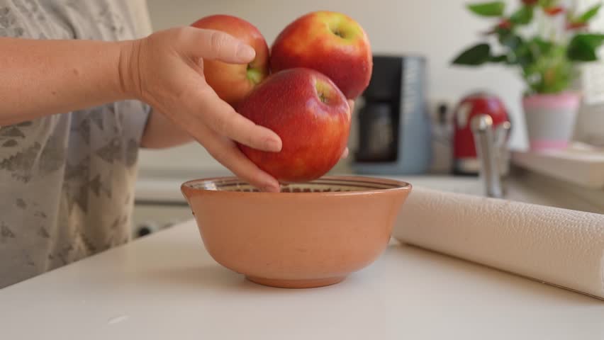 Woman puts ripe washed large red apples in ceramic bowl, in home kitchen, preparing for cooking | Shutterstock HD Video #1109166045