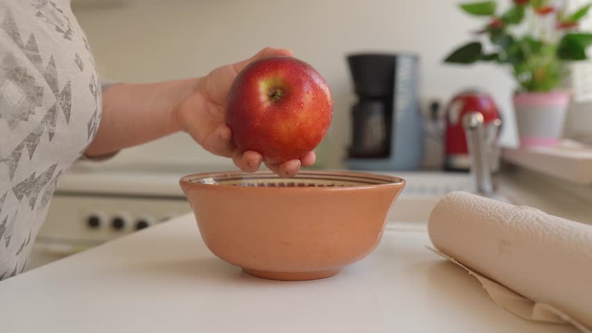 Woman puts ripe washed large red apples in ceramic bowl, in home kitchen, preparing for cooking | Shutterstock HD Video #1109166047