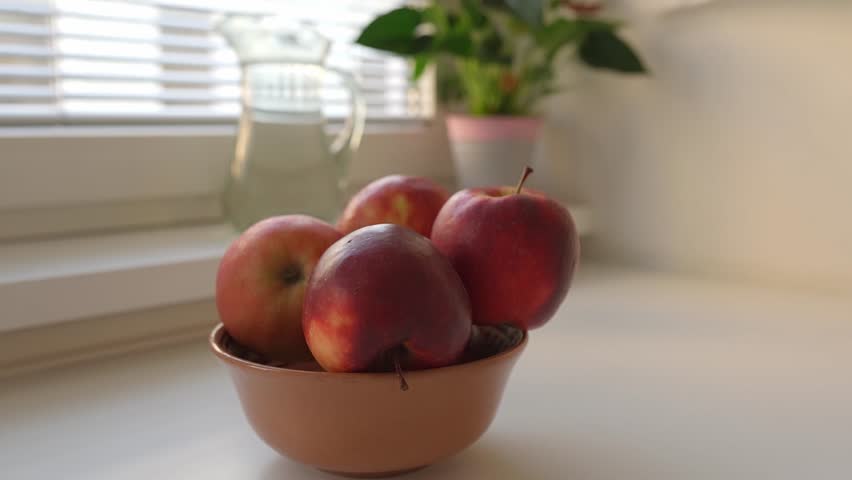 Woman puts ripe washed large red apples in ceramic bowl, in home kitchen, preparing for cooking | Shutterstock HD Video #1109166049