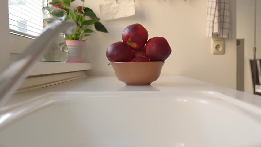Woman puts ripe washed large red apples in ceramic bowl, in home kitchen, preparing for cooking | Shutterstock HD Video #1109166051