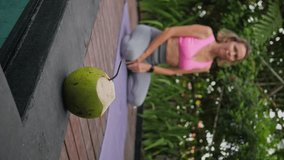Mid adult woman sitting at namaste position, green fresh coconut is ready for drinking, outdoors exercises