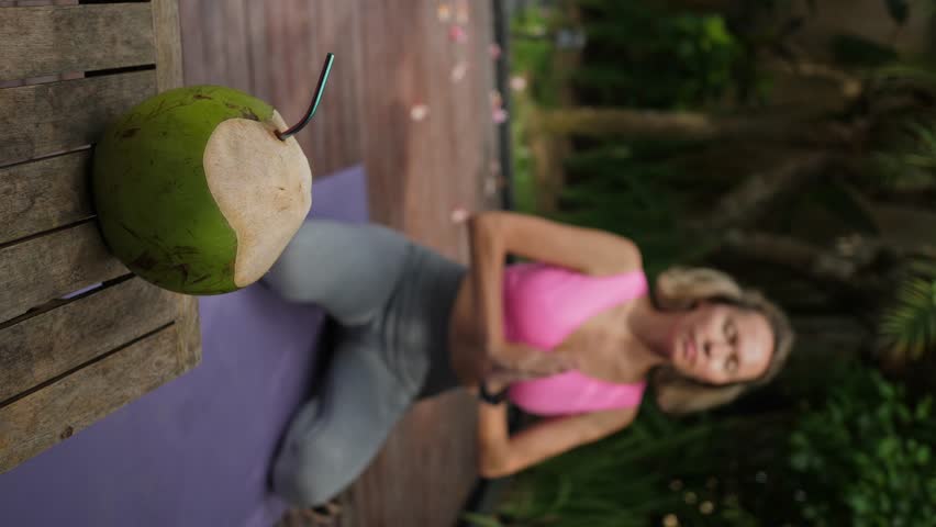 Mid adult woman sitting at namaste position, green fresh coconut is ready for drinking, outdoors exercises | Shutterstock HD Video #1109166913