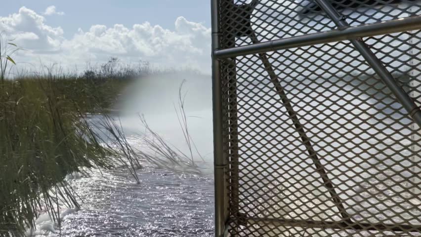 Slow motion close up shot of the back of an air boat traveling through the Florida everglades near Miami leaving a wake in the murky water surrounded by tall grass with the metal cage and propeller Royalty-Free Stock Footage #1109169827