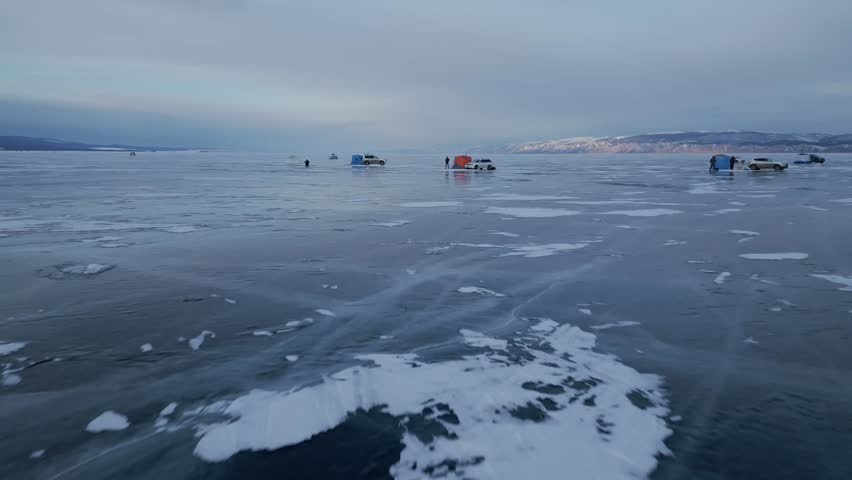 Flying a drone over tents with cars on the clear ice of Lake Baikal. Winter fishing on the largest lake