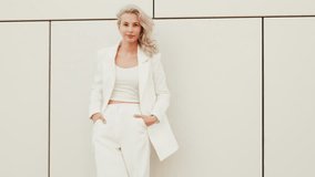 Young beautiful blond woman wearing nice trendy white suit jacket. Smiling model posing in the street at sunny day. Fashionable female outdoors. Cheerful and happy. posing near wall