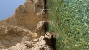 Vertical video, Panorama of beautiful rocky bay in Mediterranean Sea at Stegna beach, Rhodes island, Greece. A woman standing in water inspects coastal rocks, slow motion
