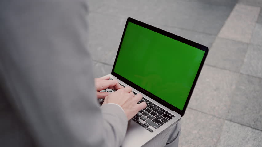 Close up of female hands typing on keyboard with portable laptop with chroma key screen. Business lady in grey suit sitting outdoors on wooden bench and working online. Copy space.