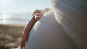 Woman hand caressing belly expecting baby close up. Unknown future mother stroking pregnant tummy sitting on sand beach at sunset. Unknown expectant mom enjoying pregnancy relaxing on evening seashore - Powered by Shutterstock - Get 15% off with code: PIKWIZARD15