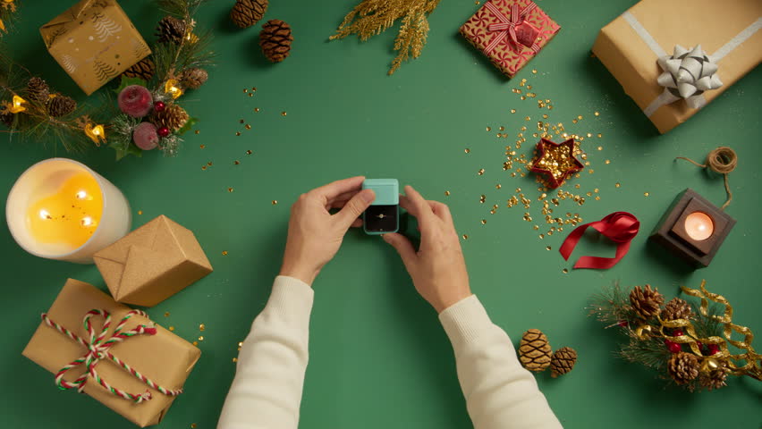 Man holds beautiful gift box with engagement ring and opens the lid. Opening light blue jewelry box on green Christmas background. Concept of gift or surprise, top down view, slow motion 4K proposal