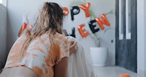 Preparing for Halloween celebration. A young woman dresses her dog in a ghost costume. Funny Halloween Moments. Decorations and Halloween party at home. Trick or treat. Stock Video
