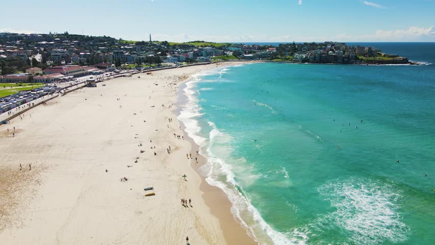 Bondi beach in Sydney, Australia. Aerial view moves along the coastline as waves crash onto the white sand where people are enjoying the beach. Royalty-Free Stock Footage #1109188447