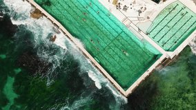 Aerial view of ocean pools at Bondi beach in Sydney, Australia. People are swimming in lanes as waves crash into the side of the pool.