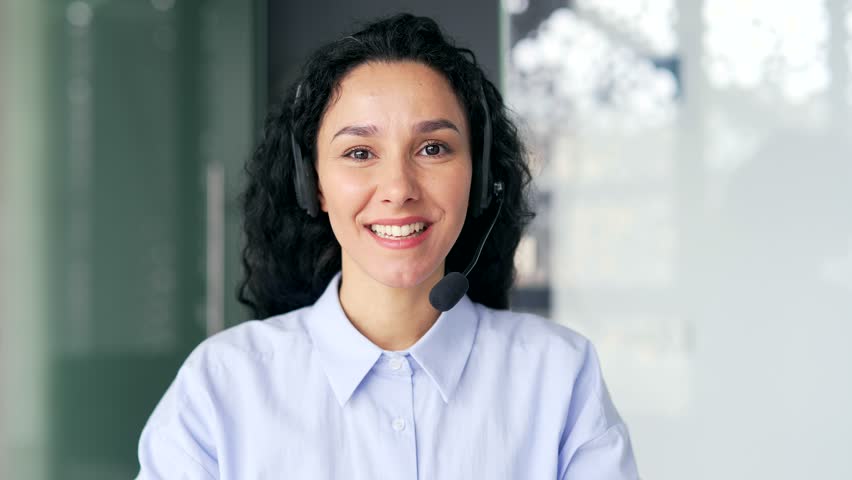 Close up. Webcam view. Woman in wireless headset customer service operator talking on video call sitting in office. Agent of the call center advises the client, answering questions looking in camera