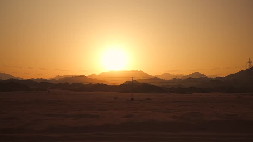 Amazing sunset in the desert with mountain range on horizon. Side view from the fast moving car by the road highway. Overhead power lines in the foreground