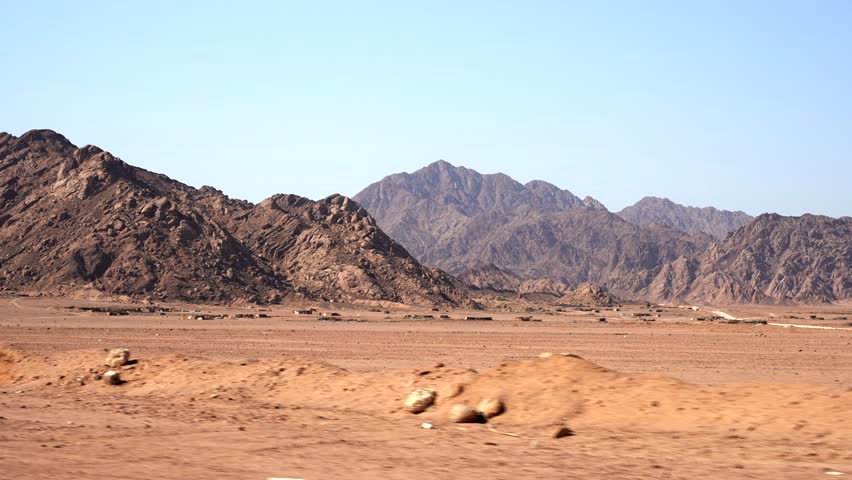 Side view from the window of moving car to the bedouin village in the desert between sandy mountains. African road trip through the Sahara
