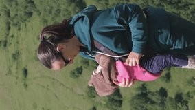 Vertical video. Young mother in sunglasses traveling with baby carrier in mountains, slow motion. Active travel with family and adventure concept