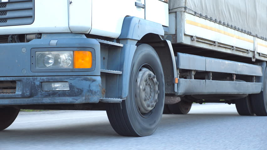 Camera follows to truck driving on a highway. Lorry rides through the countryside. Wheels of truck ride at asphalt. Close up Side view Slow motion