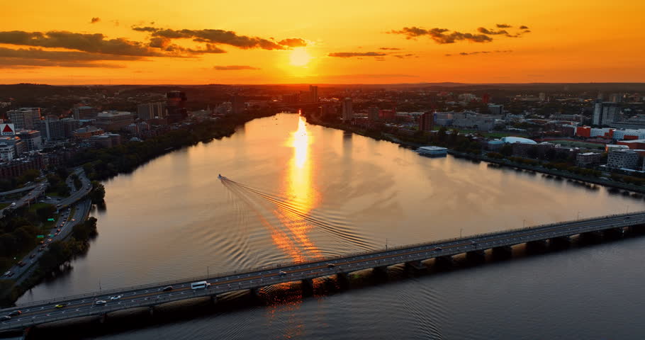 Single motor boat crossing the Charles River at sunset. Amazing scenery of Boston, Massachusetts, USA from top under orange sky.