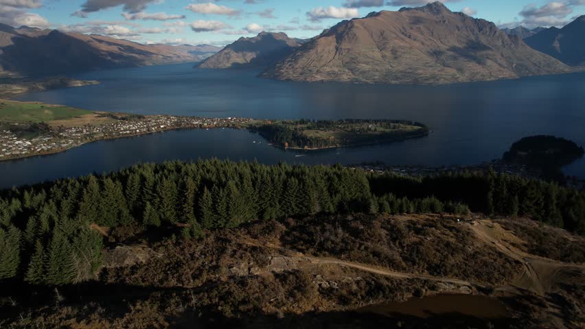 Queenstown, New Zealand aerial opening over tree line to lakeside town and mountain peak. Royalty-Free Stock Footage #1109195289