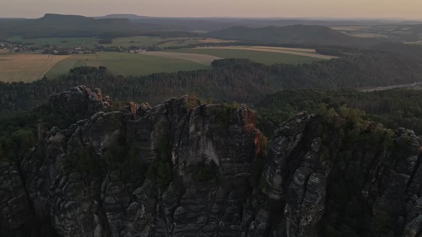 stunning outdoor landscape with a large rocky cliff in the foreground the sun is setting casting an orange and pink hue across the sky that reflects off of the mountain