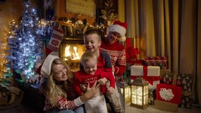 Happy family with little baby daughter, preschooler son and young beautiful parents in red Santa hats gathered together on Christmas eve near xmas tree enjoying time together at cozy fireplace RED 4K - Powered by Shutterstock - Get 15% off with code: PIKWIZARD15
