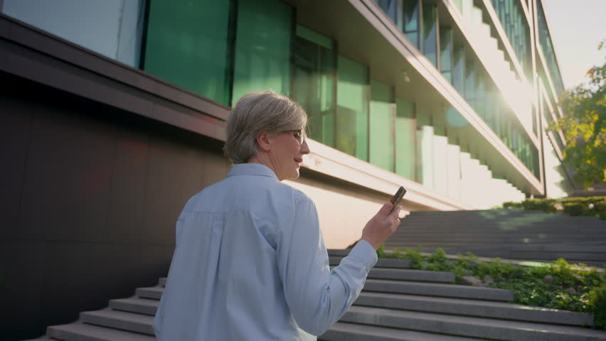 Walking outdoors Caucasian mature old woman walk city street female employer talking mobile phone business negotiate happy middle-aged businesswoman going up stairs answer smartphone call back view | Shutterstock HD Video #1109197777