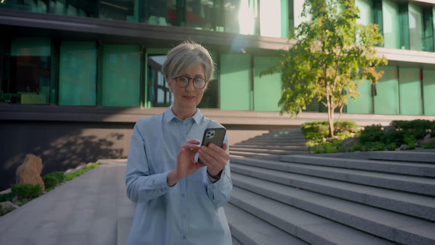Caucasian happy retired businesswoman win mobile phone online bet celebrate business success in city good news female lucky winner senior office executive delighted woman looking at camera outdoors | Shutterstock HD Video #1109197785
