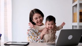 Happy together Asian mother working at home with her son. Technology communication. Looking at camera. 4k slow motion.