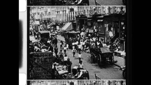 1915 NYC. Street scene. Young kid operates hand cranked carousel. Vendors sell goods. Bustling city with authentic people. Vintage NYC from early 20th Century. 4K Overscan of archival newsreel film  Video Stok Editorial