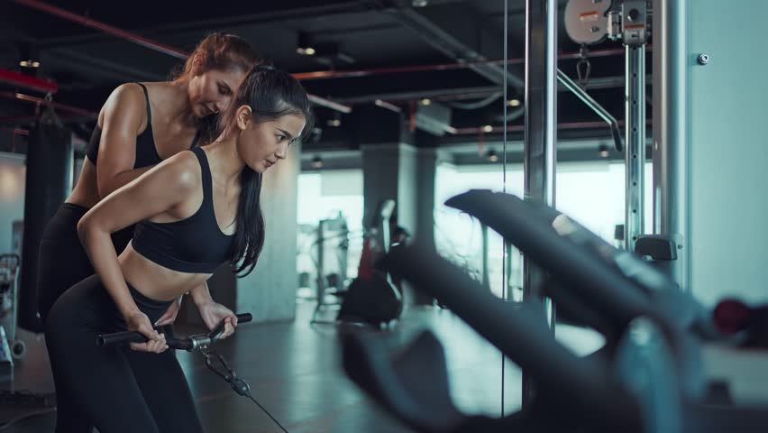 Young Asian woman doing exercises in fitness gym, exercises to strengthen muscles and strength with personal trainer. Fitness exercising in gym. - Powered by Shutterstock - Get 15% off with code: PIKWIZARD15
