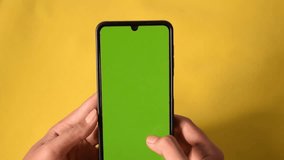 two hands hold a smartphone and scrolling the screen, green screen isolated on yellow background