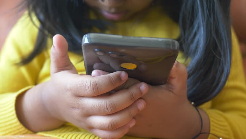 Child in yellow dress girl watching cartoon on smart phone 