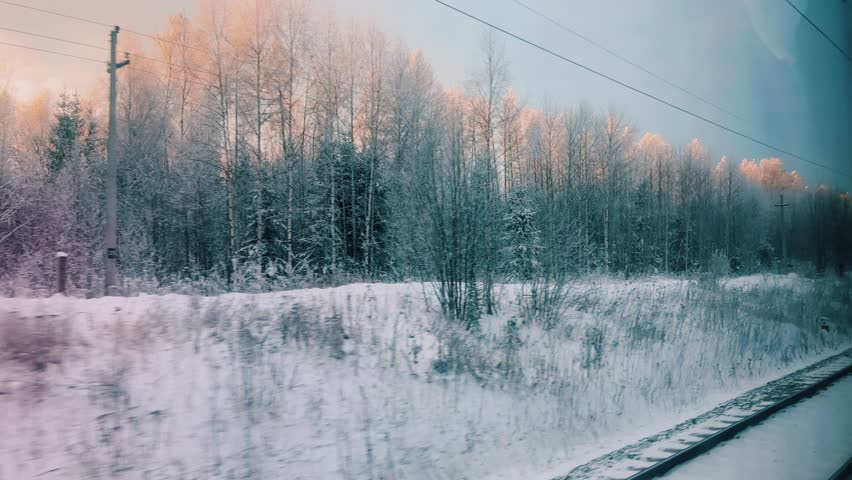 Winter train journey. Houses and winter forest flash by the window. View from the train window on the winter landscape. Winter sunset from the train window. Russia 2023