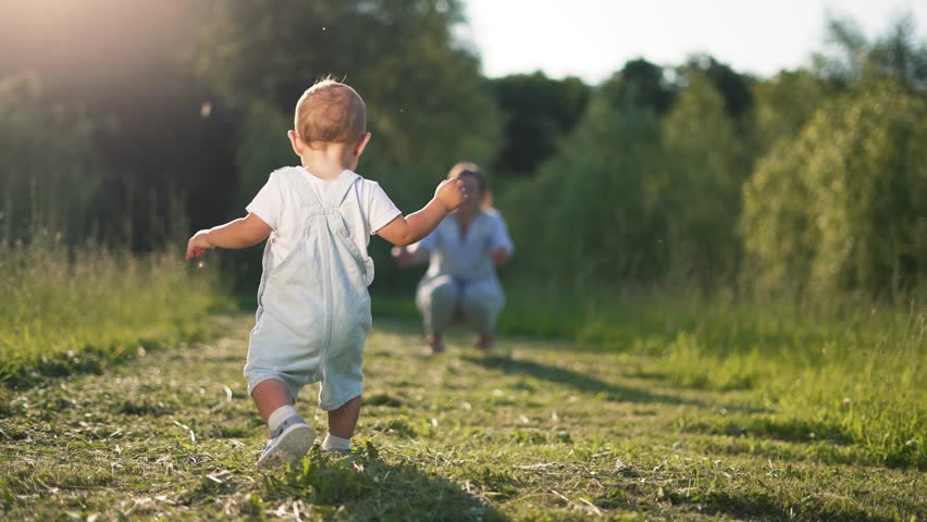 First steps. Childhood dream concept. Happy family in park on green grass. Mom teaches baby to take first steps. Happy mother day the first steps of cheerful kids in park on grass. First steps concept