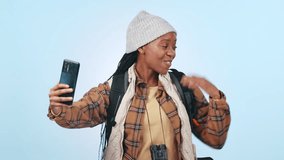 Hiking, video call and black woman with hand pointing to mockup in studio for travel or adventure on blue background. Backpacking, journey and African lady influencer live streaming blog or podcast