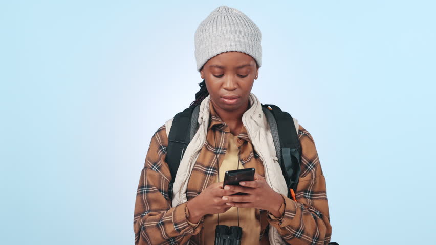 Phone, search and black woman hiking in studio happy for location satisfaction on blue background. Smartphone, guide and African female hiker with app for map, direction or navigation while traveling Royalty-Free Stock Footage #1109209439
