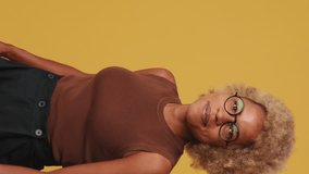 Vertical video, Happy friendly girl in glasses, wearing a brown top showing double thumbs up smiling and looking at the camera, isolated on background, studio shot