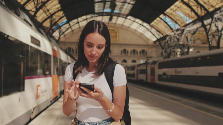 Beautiful girl traveler uses mobile phone while standing on the platform of the railway station