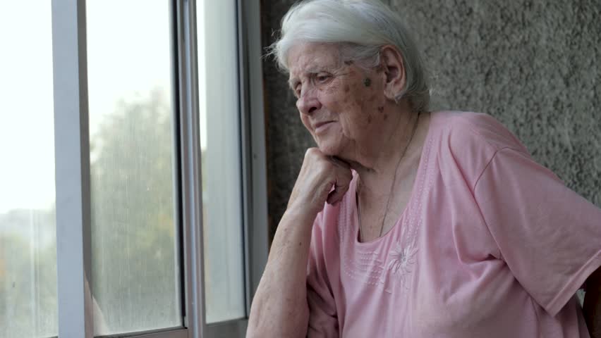 Portrait sad old woman hope looks out window at street through glass. Worrying or missing family relatives. Lonely people in elderly age in nursing homes. Suffers nervous tics and tremor hands Royalty-Free Stock Footage #1109220571