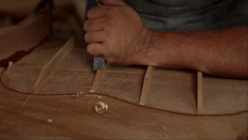 This close-up footage shows a guitar luthier using a chisel to shave the bracing of an acoustic guitar. The luthier is carefully working to ensure that the braces are the correct shape and size.