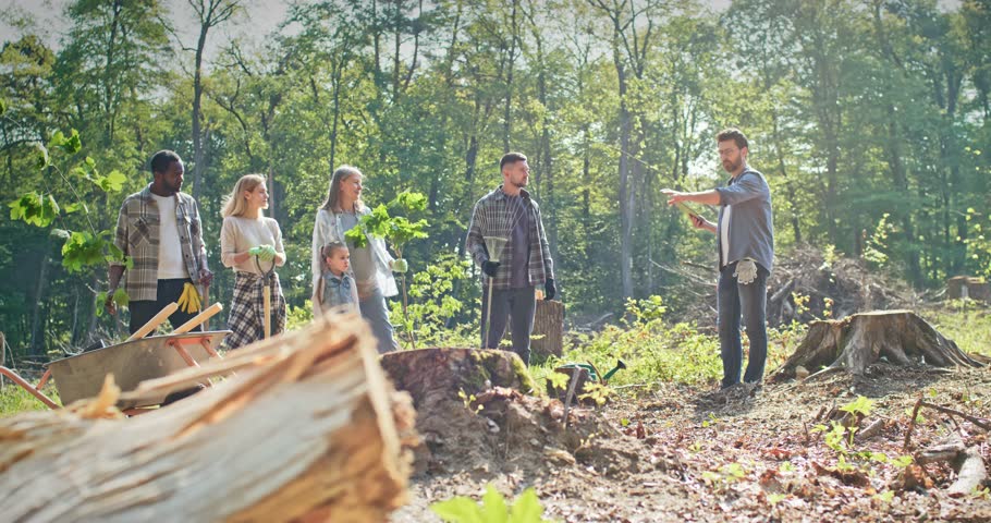 Group of happy people kids and adults listening to instructions from leader. Enthusiastic volunteers planting trees in forest. Environment activists providing forestation work. Nature concept.