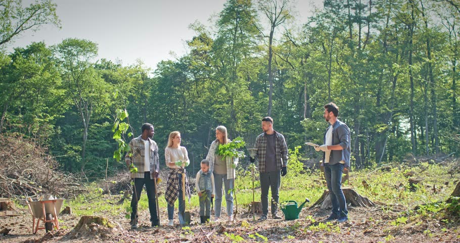 Side view of happy enthusiastic attractive multiage group of people doing forestation work helping nature. Nature conservationists planting trees in woods taking care of environment and ecology.