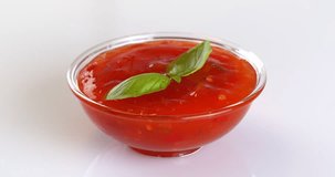 Close-up footage of a glass bowl with sweet chili sauce and basil on a rotating table on a white background.