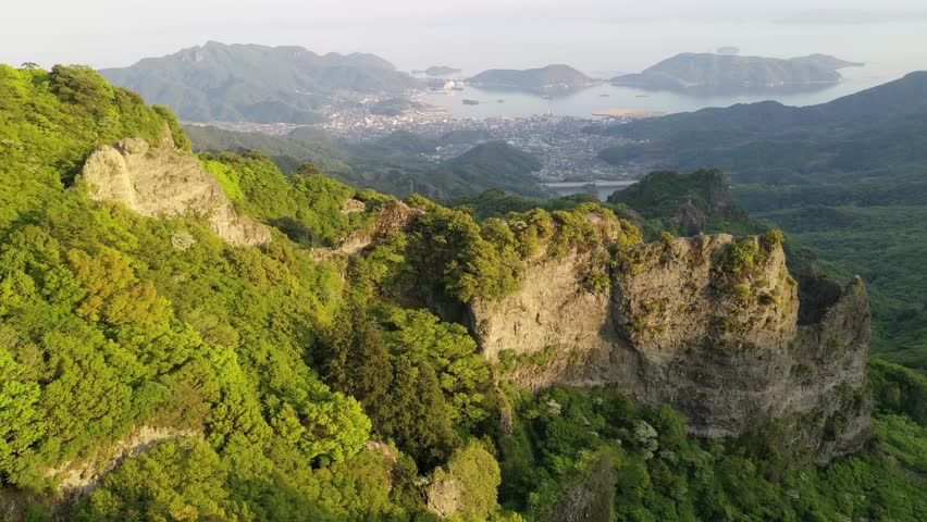 Aerial view from Takatori Viewpoint overlooking rugged cliffs and green forests of Kankakei Gorge on Shodoshima Island with a village on the coastline and islets in Seto Inland Sea, in Kagawa, Japan