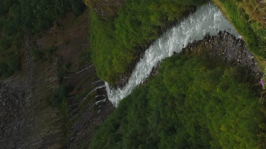 A stormy mountain river Terek with small narrow waterfalls in the valley of the Truso gorge. Nature of Georgia. Beautiful green forest in early autumn. Vertical slow motion 4k footage