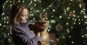Portrait of happy woman with a red cat in her hands on the background of a Christmas tree. 4k video