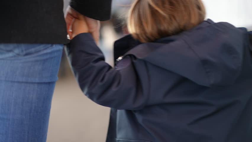 Back of small boy holding hands with mother walking while on commute travel, child wearing jacket