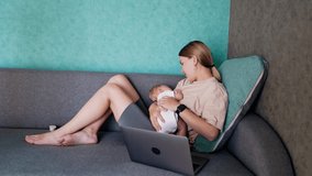 New-made mom with baby in hands sits on sofa. Caucasian woman working remote at home combining work and childcare.