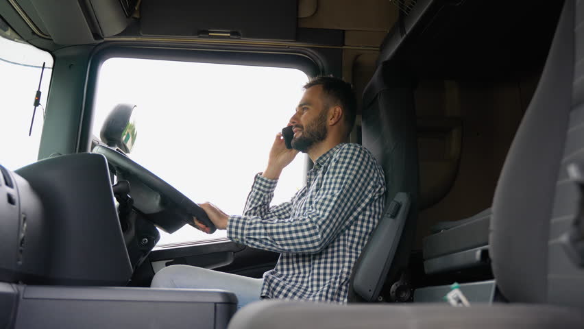 Truck driver talking by mobile phone while sitting in cabin of his truck. Right hand drive car Royalty-Free Stock Footage #1109240881