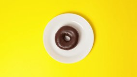 Eating delicious sweet donut covered with chocolate glaze on bright yellow background. Stop motion food donut animation video. Bakery and food concept. Top view of chocolate doughnut in 4K